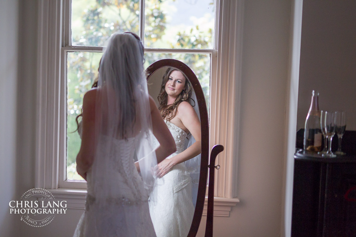 bride looking wearinf wedding dress looking in mirror - pre wedding photos - wedding photo ideas - getting ready wedding pictures - bride - groom - wedding dress - wedding detail photos - wilmington nc wedding photography
